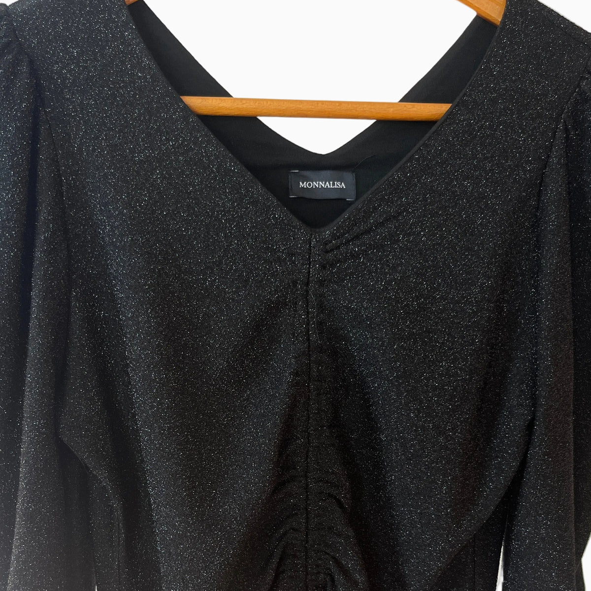 Dettaglio collo a V abito nero Monnalisa con etichetta interna e texture lurex scintillante