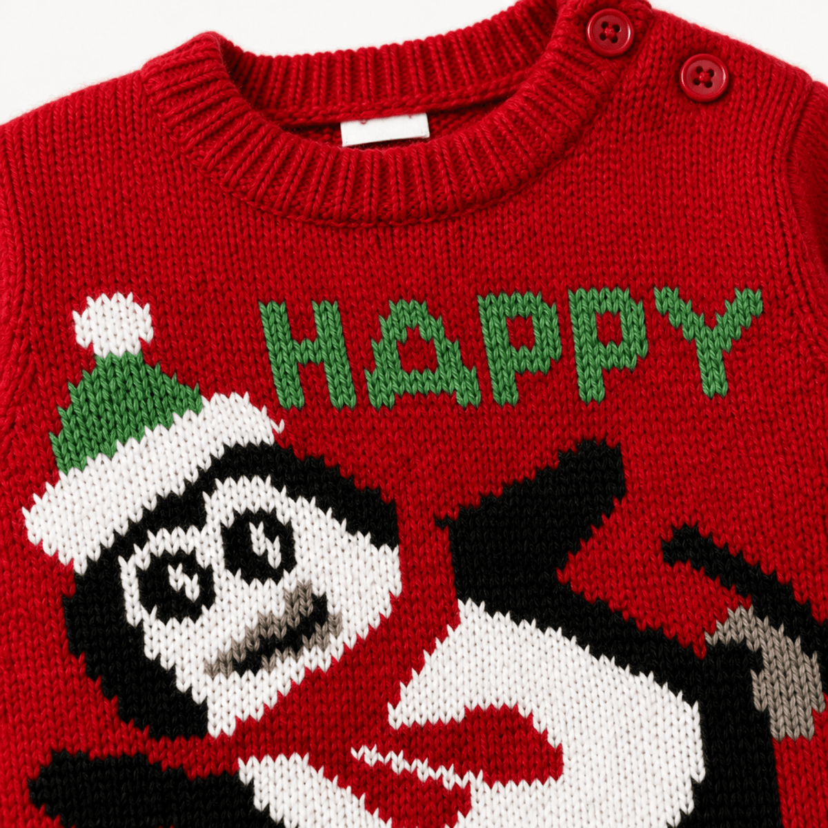 Dettaglio tessuto maglione natalizio rosso neonato pinguino e scritta HAPPY